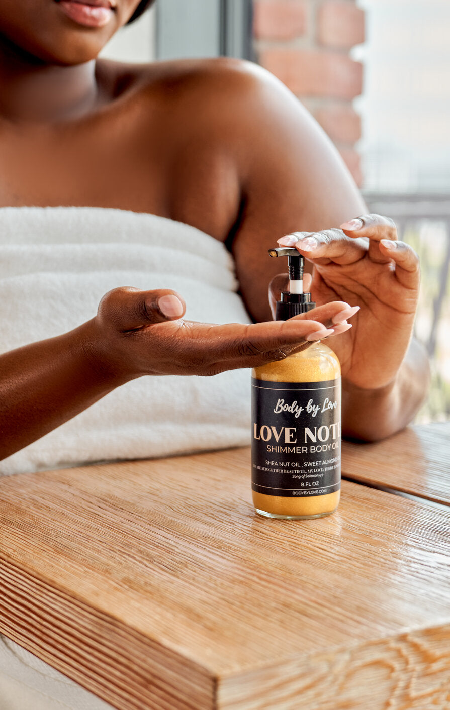 Plus size woman in oversized bath towel from brand Body by Love using Love notes shimmer body oil after the shower.